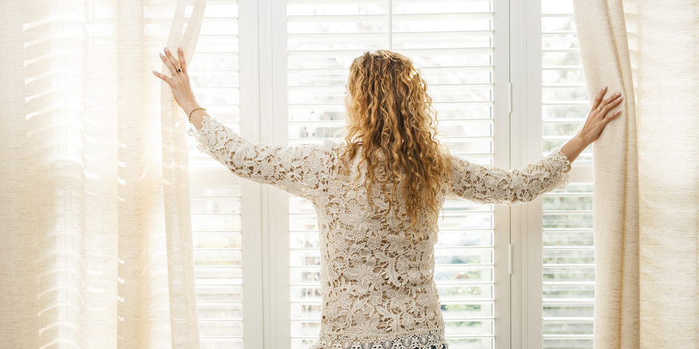 Woman opening blinds to let light in
