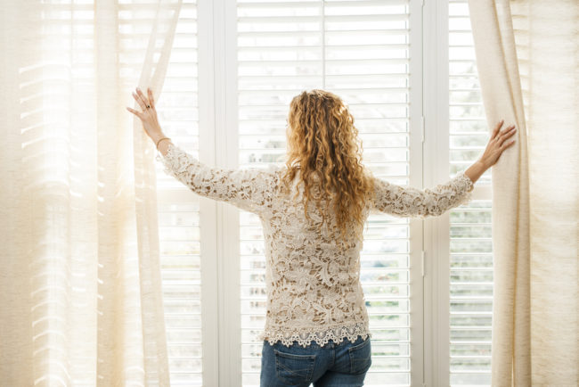 Woman opening blinds to let light in